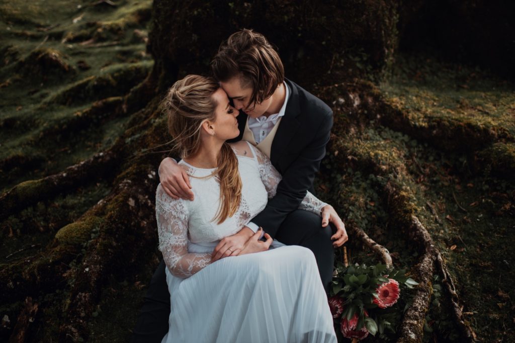 Una foto dell'elopement di Klara e Siddy realizzato da Fabio Miglio, tra i fotografi di matrimonio a Torino iscritti ad ANFM: i due sposi sono seduti alle radici di un albero e si abbracciano