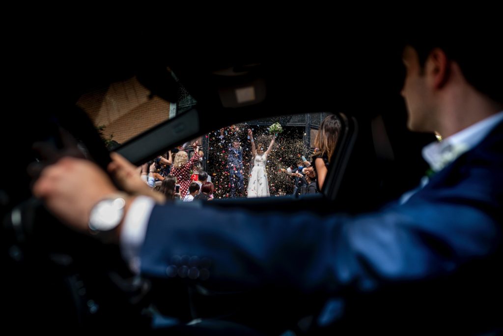 Una foto realizzata dal finestrino di un'auto mentre gli sposi escono dalla Chiesa dopo il sì, avvolti dai coriandoli: lo scatto è di Marina di Rosi di Cromatica Foto, tra i migliori fotografi di matrimonio a Torino