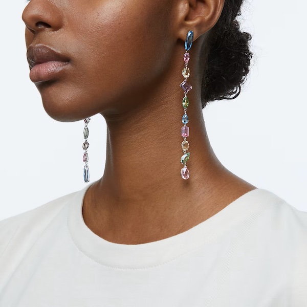 In questa foto una modella indossa un paio di pendenti lunghi, realizzati con pietre dure colorate, della collezione gioielli donna 2023 Swarovski