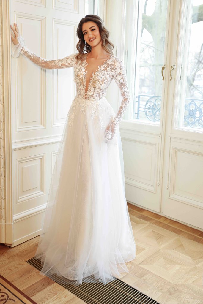 In questa immagine un abito da sposa Annais Bridal con corpetto in pizzo, maniche lunghe ricamate e gonna in tulle.