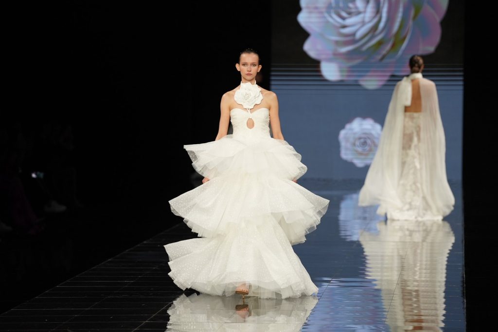 In questa immagine una modella indossa un abito da sposa Isabel Sanchis 2024 con gonna ampia arricchita da maxi Rouches.