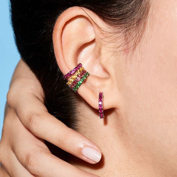 In questa foto una modella indossa su un unico orecchio un orecchino a cerchio piccolo con pietre fucsia e quatto earcuffs in fucsia, giallo, rosso e verde. Si tratta di una grandissima tendenza in fatto di gioielli donna 2023. La proposta in foto è di Poesia Gioielli