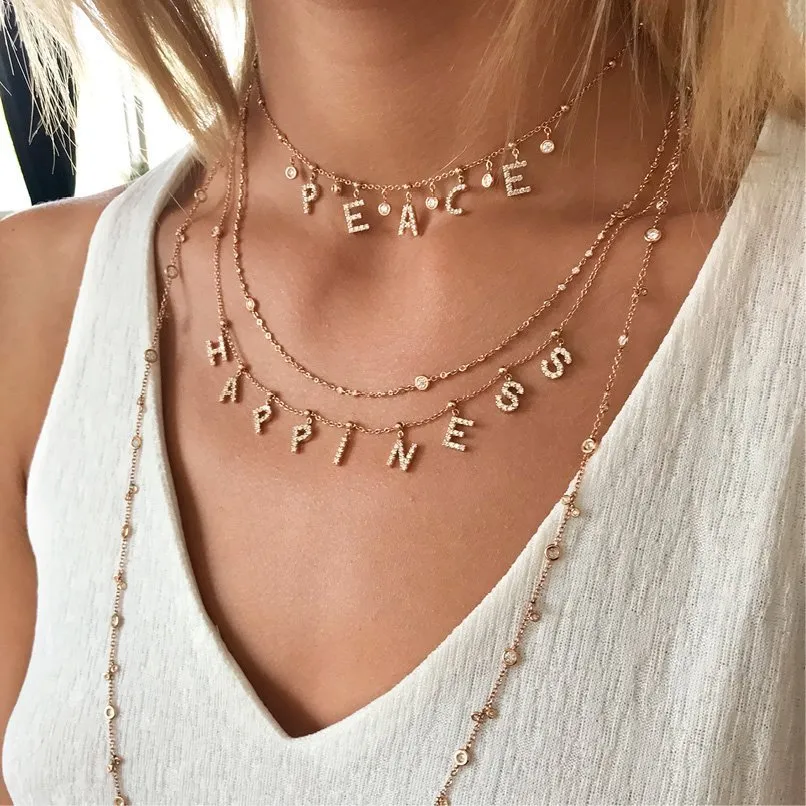 In questa foto una modella mostra un Layering sul décolleté, realizzato con diversi fili di collane in oro giallo di Crivelli. Alcune delle collane riportano come ciondoli delle lettere che ricreano le parole "peace" e "happiness" 