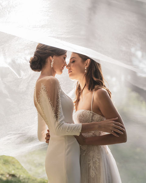 In questa foto le due spose della campagna Love is Love di Pronovias indossano due abiti dell'azienda: uno a sirena in chiffon con maniche lunghe e uno scivolato in tulle con ricami floreali