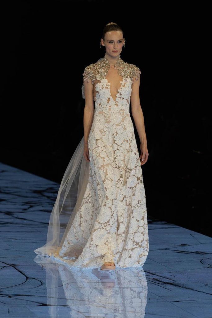 In questa foto una modella sfila indossando un abito da sposa in pizzo floreale con scollatura a V e ricami gioiello sulle spalle