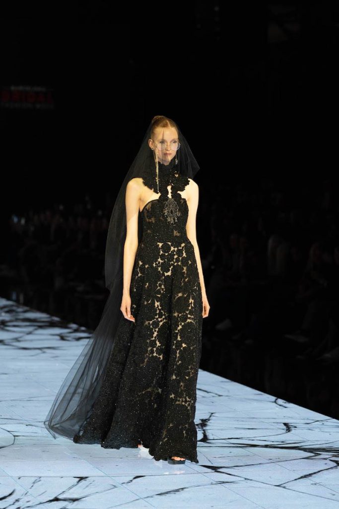 In questa foto una modella sfila indossando un abito da sposa di colore nero in pizzo floreale, con scollatura girocollo e velo abbinato