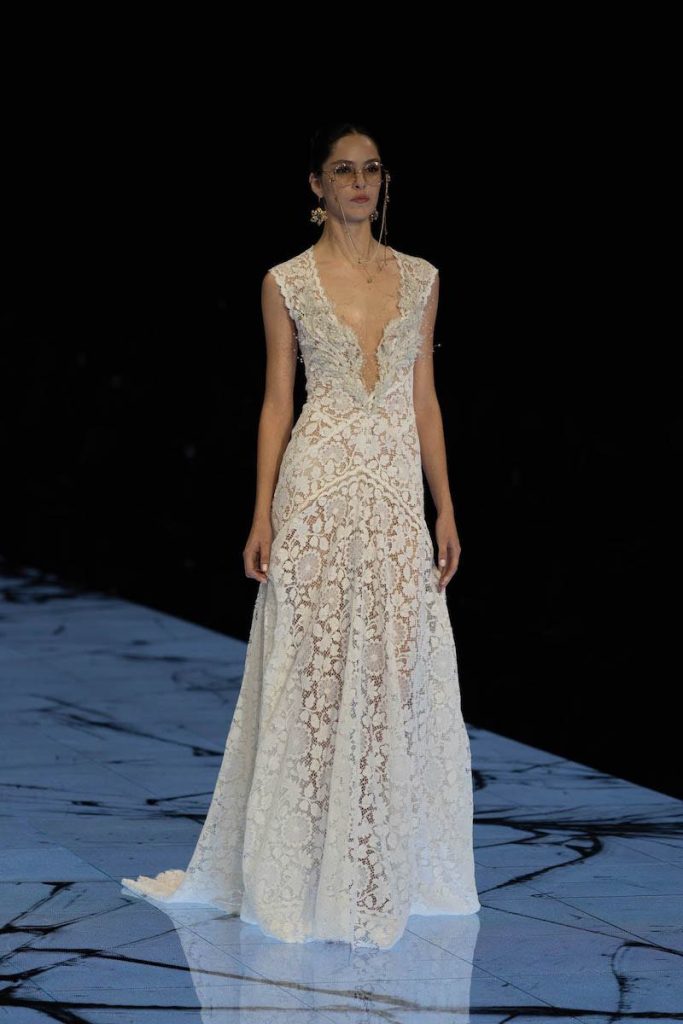 In questa foto una modella sfila indossando un abito da sposa Marco y Maria 2024 scivolato con scollatura profonda 