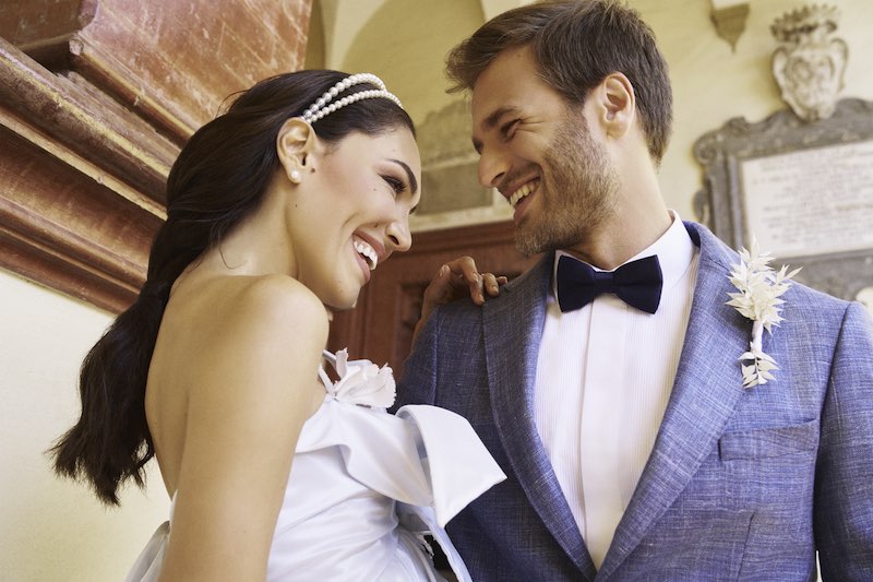 In questa foto due sposi si guardano e si abbracciano sorridenti. Indossano due abiti di colore azzurro e turchese