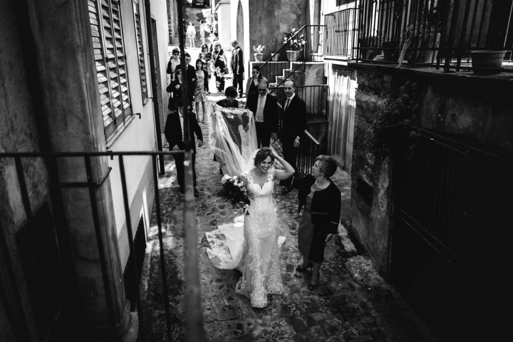 In questa foto realizzata da Alberto Cosenza, tra i fotografi di matrimonio a Reggio Calabria, la sposa si dirige verso la Chiesa mentre altre donne le tengono il velo