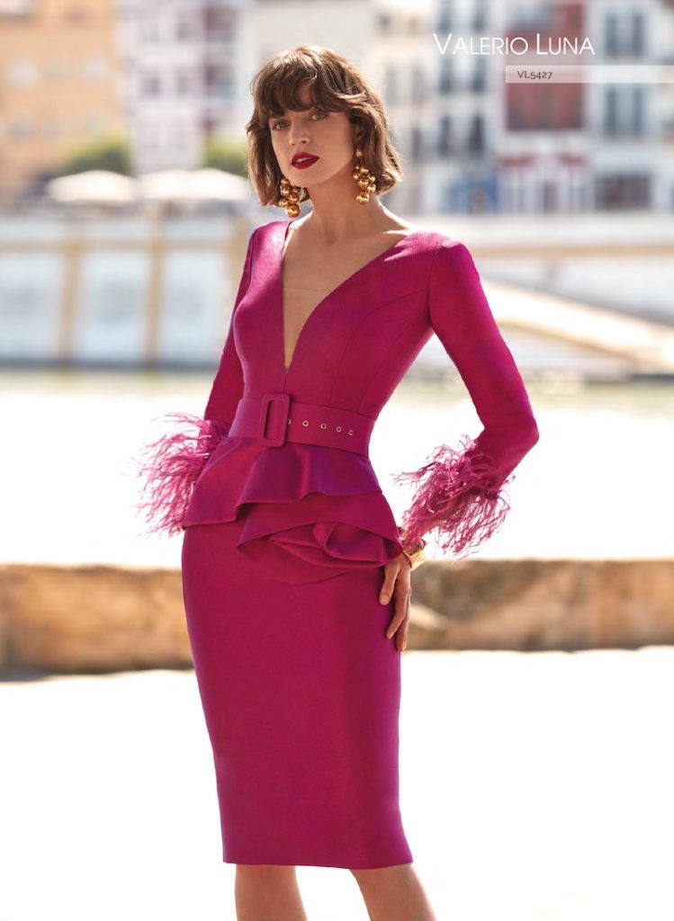 In questa foto una modella posa indossando un abito midi modello longuette di Valerio Luna con maniche, plumage ai polsi e cintura in vita di colore fucsia per un look Barbiecore da cerimonia