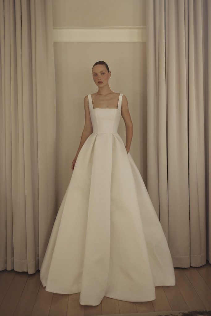 In questa foto una modella posa indossando un abito da sposa ad A in taffetá con scollo quadrato di Lihi Hod