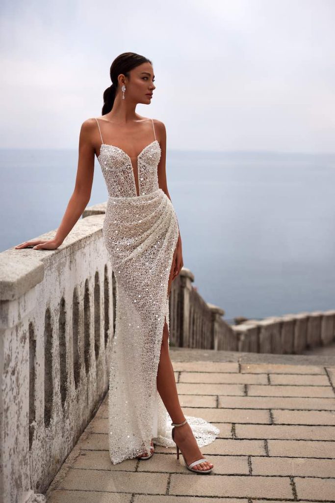In questa foto una modella posa indossando un abito da sposa con tessuto sparkling di Julie Vino con spacco profondo sul lato sinistro