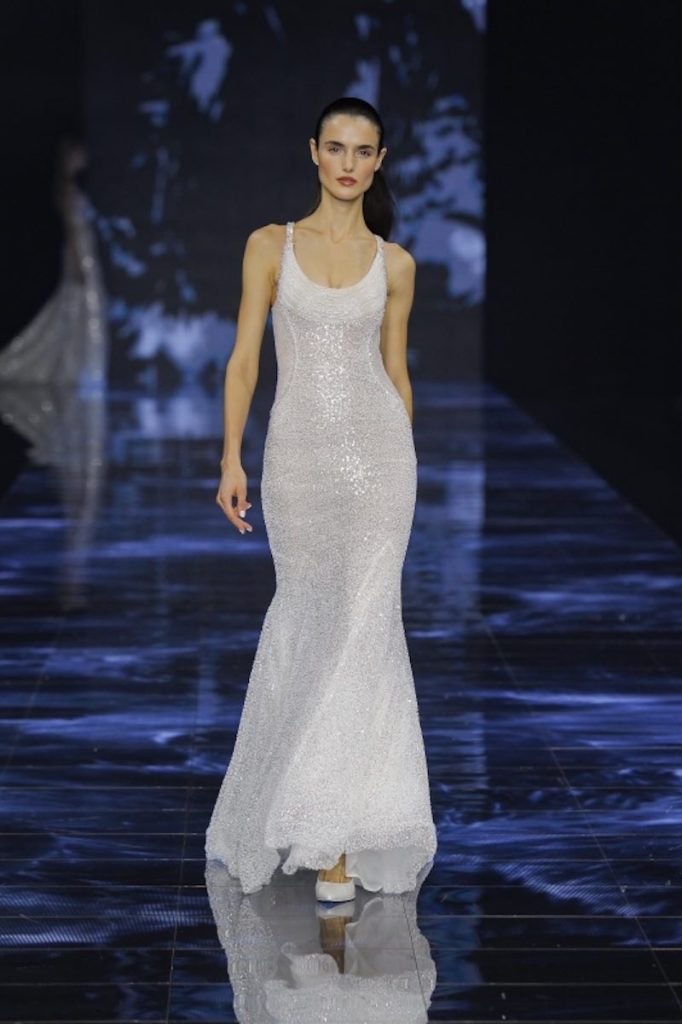 In questa foto una modella sfila indossando un abito da sposa modella a sirena con tessuto glitter e scollo rotondo di Pronovias 