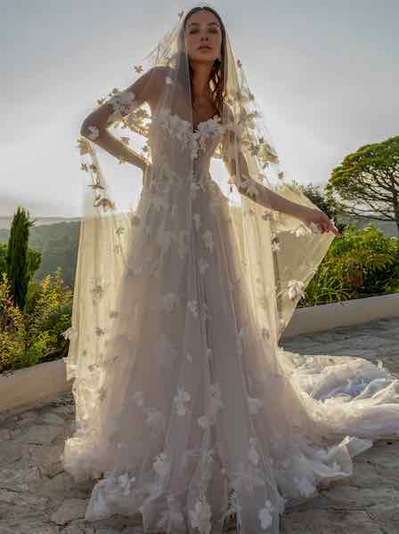 In questa foto una modella posa indossando un abito da sposa ad A di Diane Legrand con elementi flroeali 3D e velo abbinato