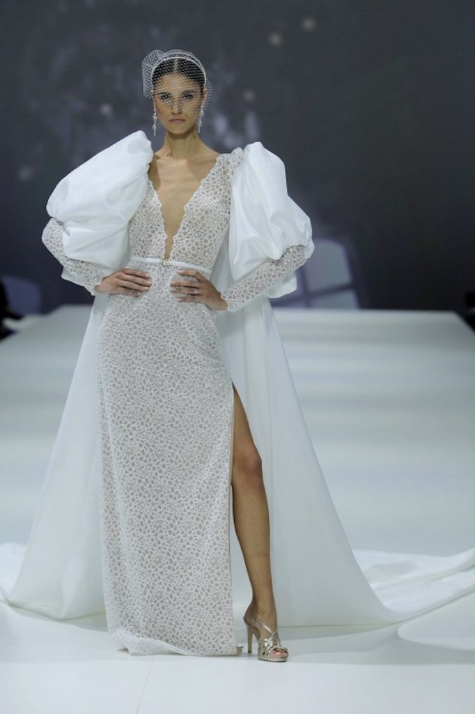 In questa foto una modella sfila indossando un abito da sposa di Agnieszka Swiatly di pizzo maccramé con scollo a v e spalline di satin oversize