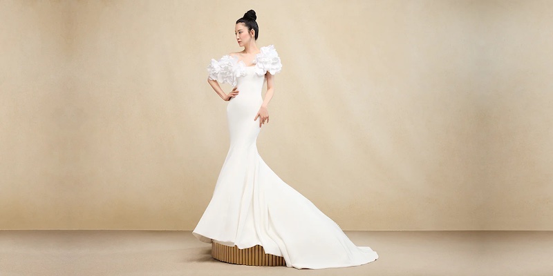 In questa foto una modella posa su un piedistallo indossa un abito da sposa di Ines Di Santo modello semisirena con maxi spalline floreali
