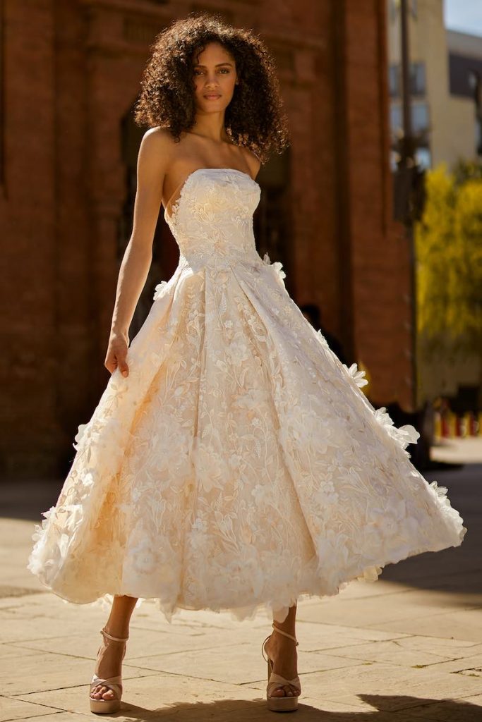 In questa foto una modella posa indossando un abito da sposa midi di Ines Di Santo con scollatura dritta ed elementi floreali 3D