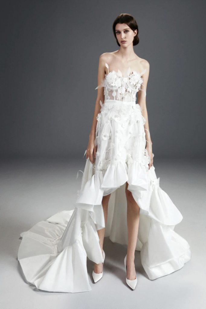 In questa foto una modella posa indossando un abito da sposa mullet di Viktor&Rolf in taffetá con rouches sull'orlo e applicazioni floreali 3D