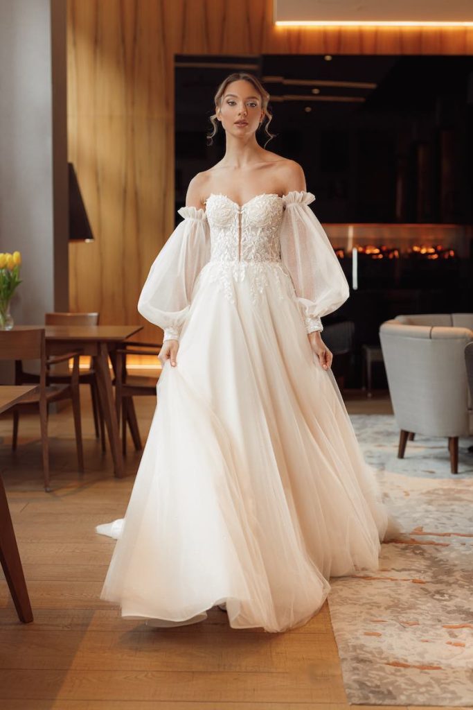 In questa foto una modella posa indossando un abito da sposa ad A Annais Bridal in chiffon con corpetto ricamato e maniche a sbuffo removibili