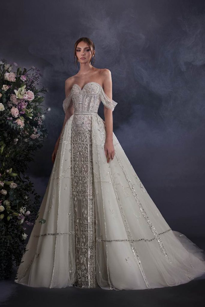 In questa foto una modella posa indossando un abito da sposa di Elie Saab con ricami di perline e paillettes e sovragonna di tulle ricamato con paillettes
