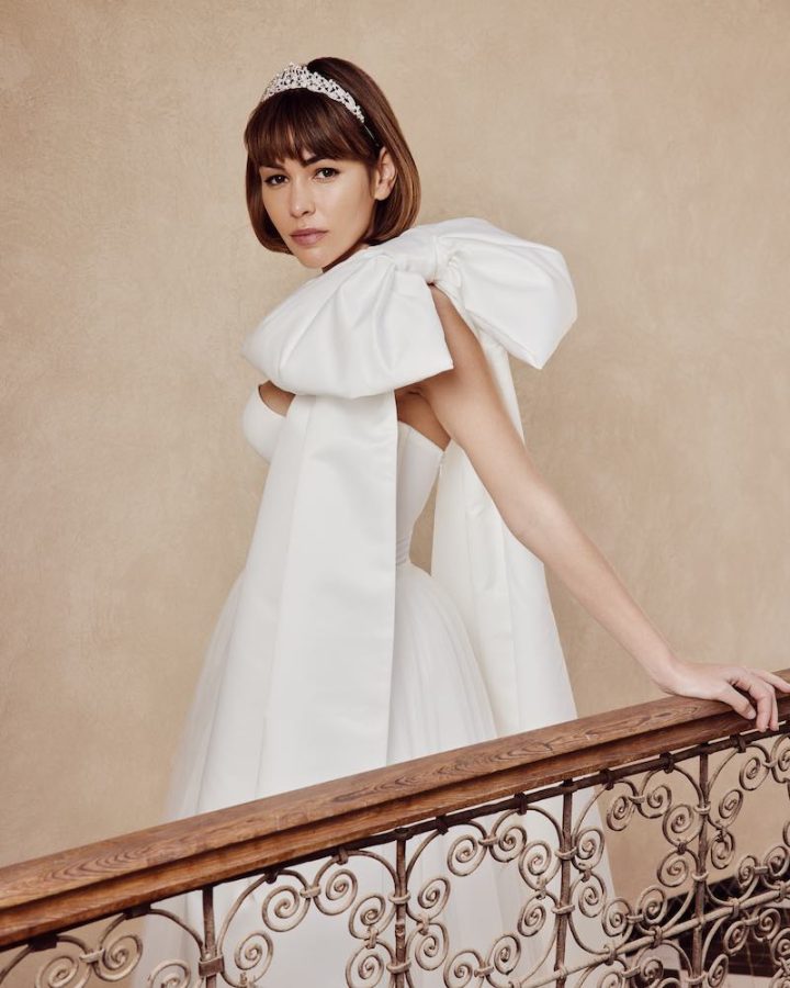 In questa foto una modella posa sulle scale indossando un abito da sposa di Poirier con maxi fiocco sulla spalla sinistra