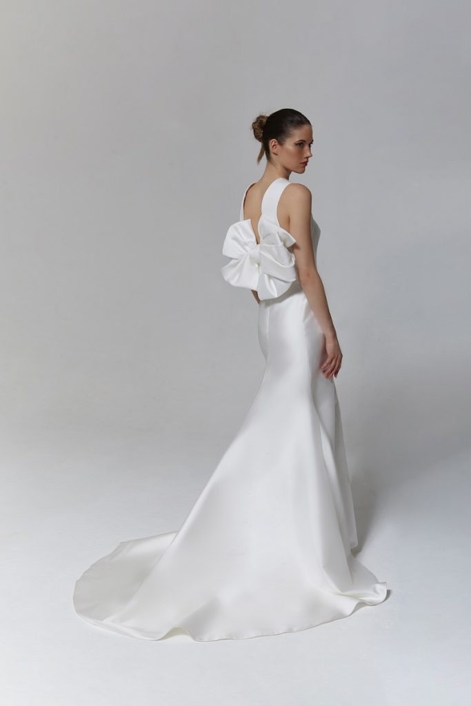 In questa foto una modella posa di spalle indossando un abito da sposa in satin di Tosca Spose con maxi fiocco sulla schiena