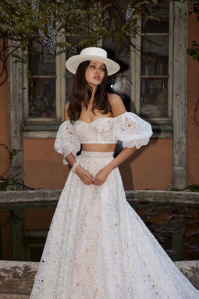In questa foto una modella posa indossando un abito da sposa crop top con maniche balloon in pizzo Sangallo di Flora