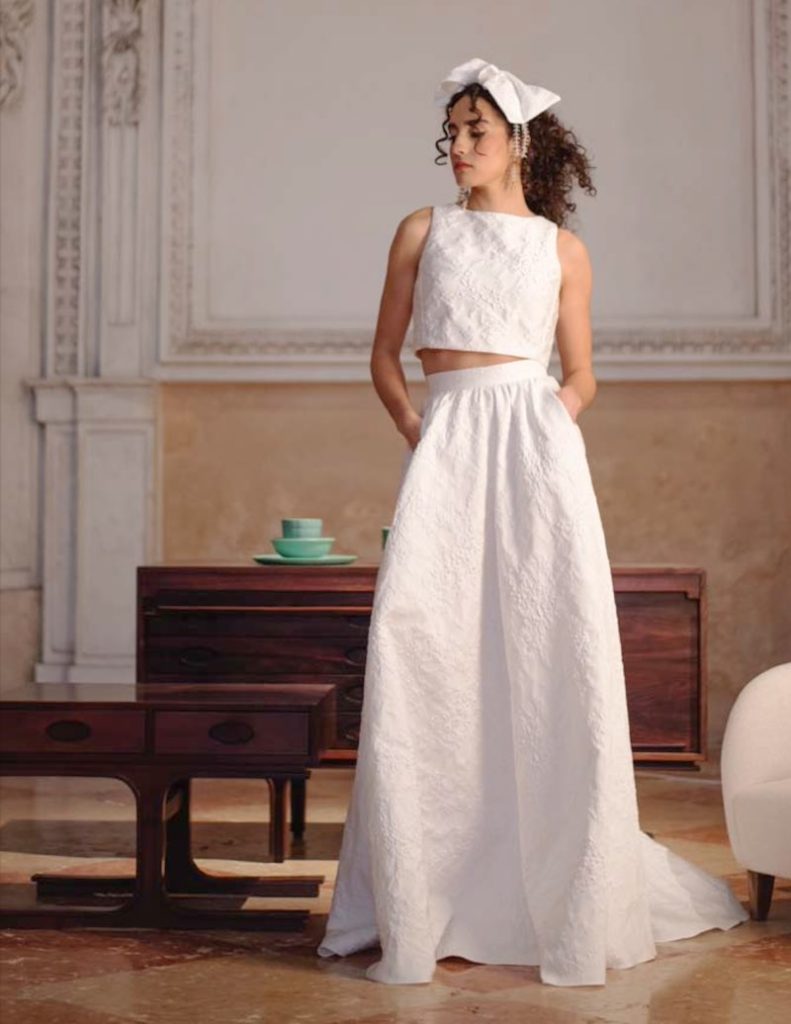 In questa foto una modella posa indossando un abito da sposa due pezzi con crop top di Poesie Sposa 