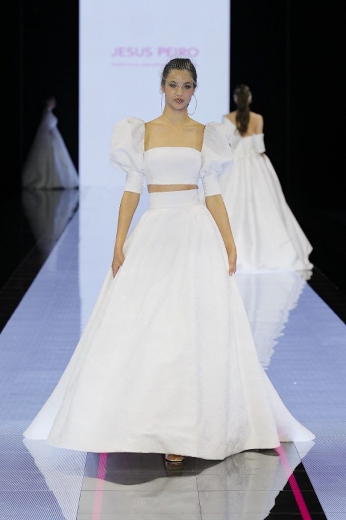 In questa foto una modella sfila indossando un abito da sposa due pezzi con crop top di taffetá con maniche corte balloon 
