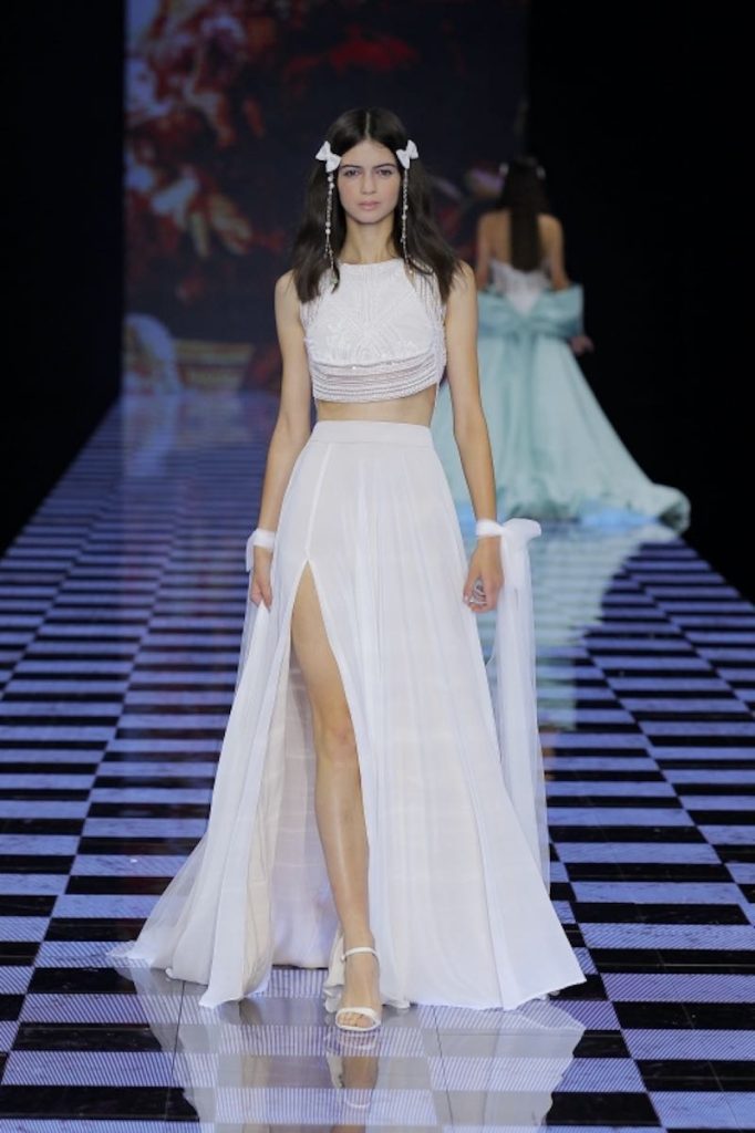 In questa foto una modella sfila indossando un abito da sposa due pezzi con crop top di Lorena Panea. La gonna presenta uno spacco sul fianco destro