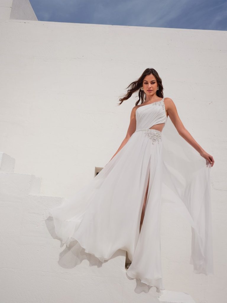 In questa foto una modella posa indossando un abito da sposa in organza voile di Mysecret Sposa con leggero cut out sul fianco sinistro, spacco frontale, scollo obliquo