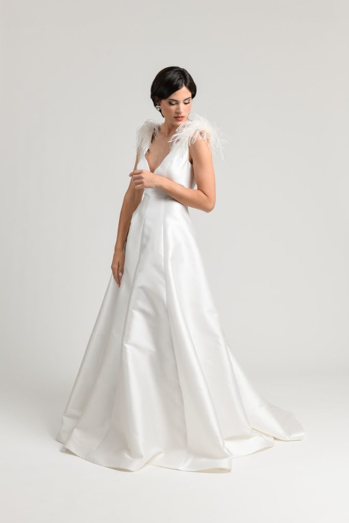 In questa foto una modella posa indossando un abito da sposa di Atelier Benedetta in mikado con scollo a V e dettagli plumage sulle spalle
