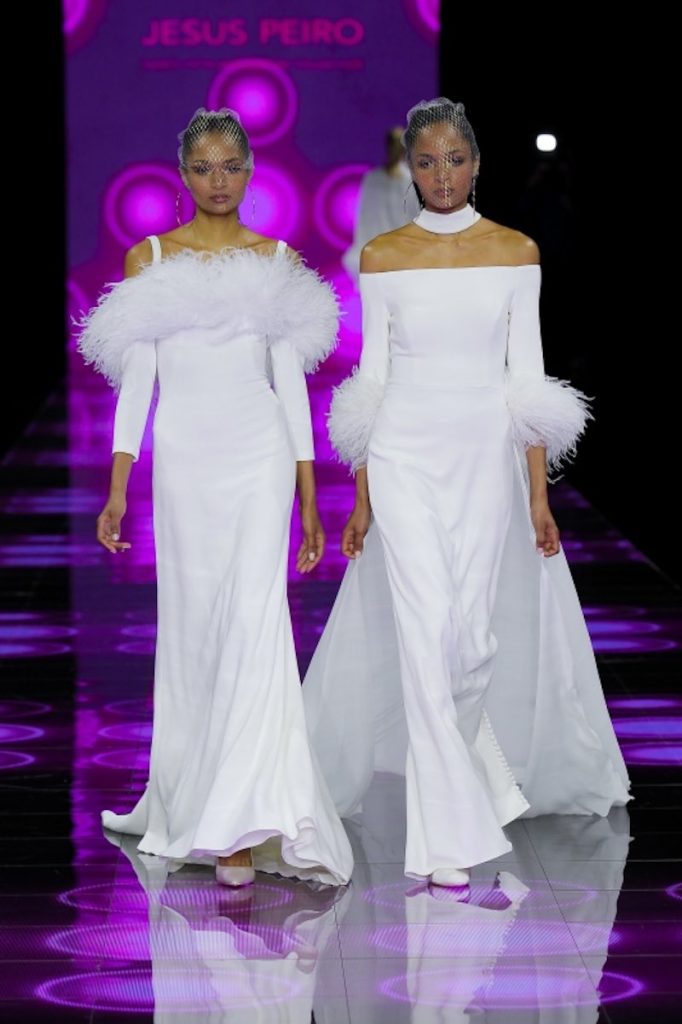 In questa foto due modelle sfilano indossando due abiti da sposa scivolati in cady di seta con bordo plumage sulla scollatura e sui polsiini 