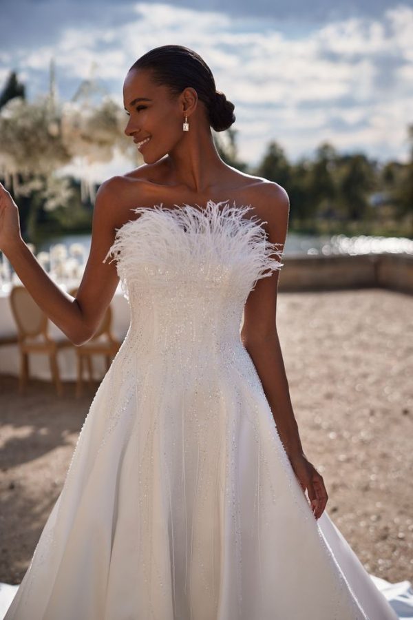In questa foto una modella posa a mezzo busto indossando un abito da sposa di Milla Nova a trapezio con corpetto con paillettes e plumage 
