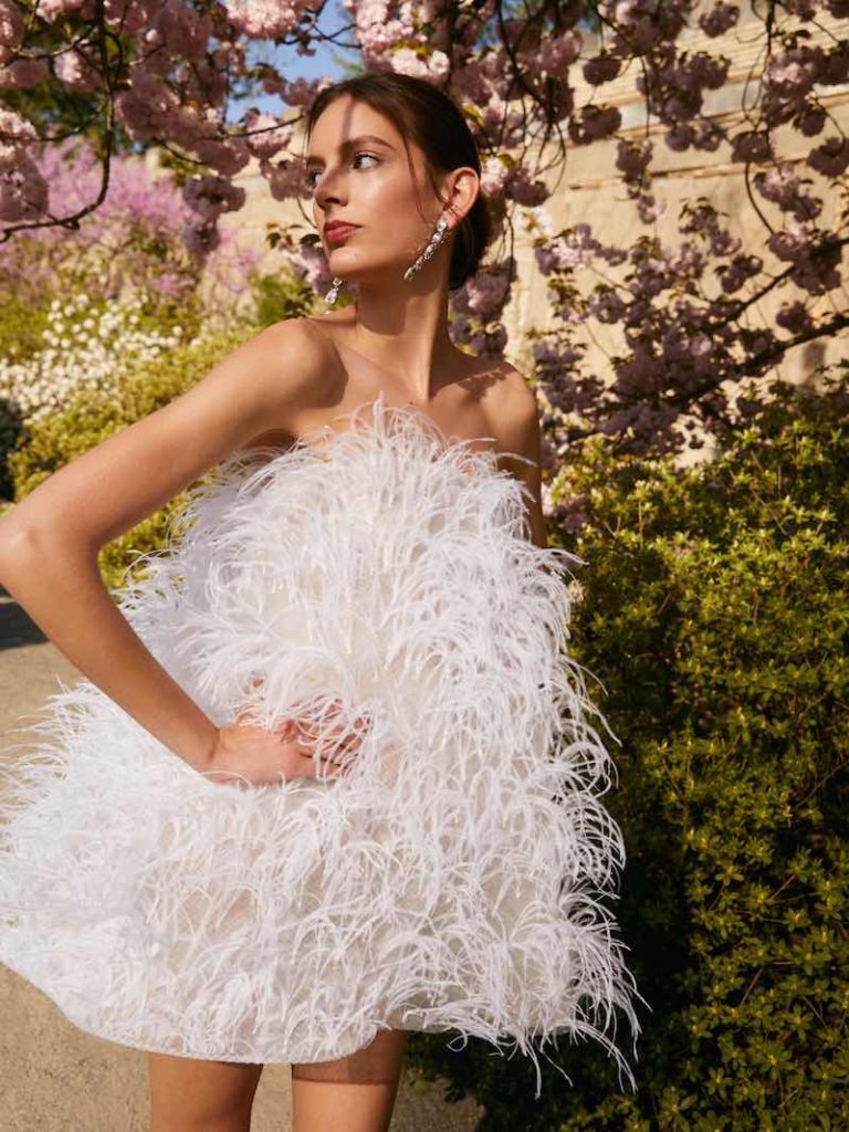 In questa foto una modella posa indossando un abito da sposa corto con piume all over di Oscar de la Renta