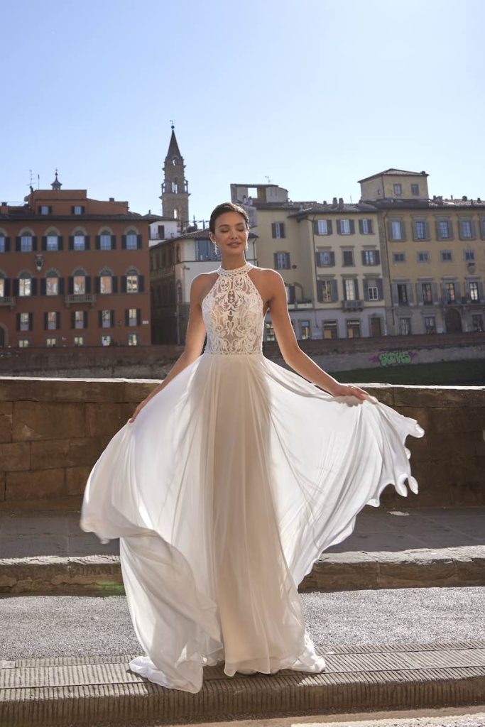 In questa foto una modella posa indossando un abito da sposa scivolato in chiffon di Diane Legrand con corpetto di pizzo e scollo all'americana 