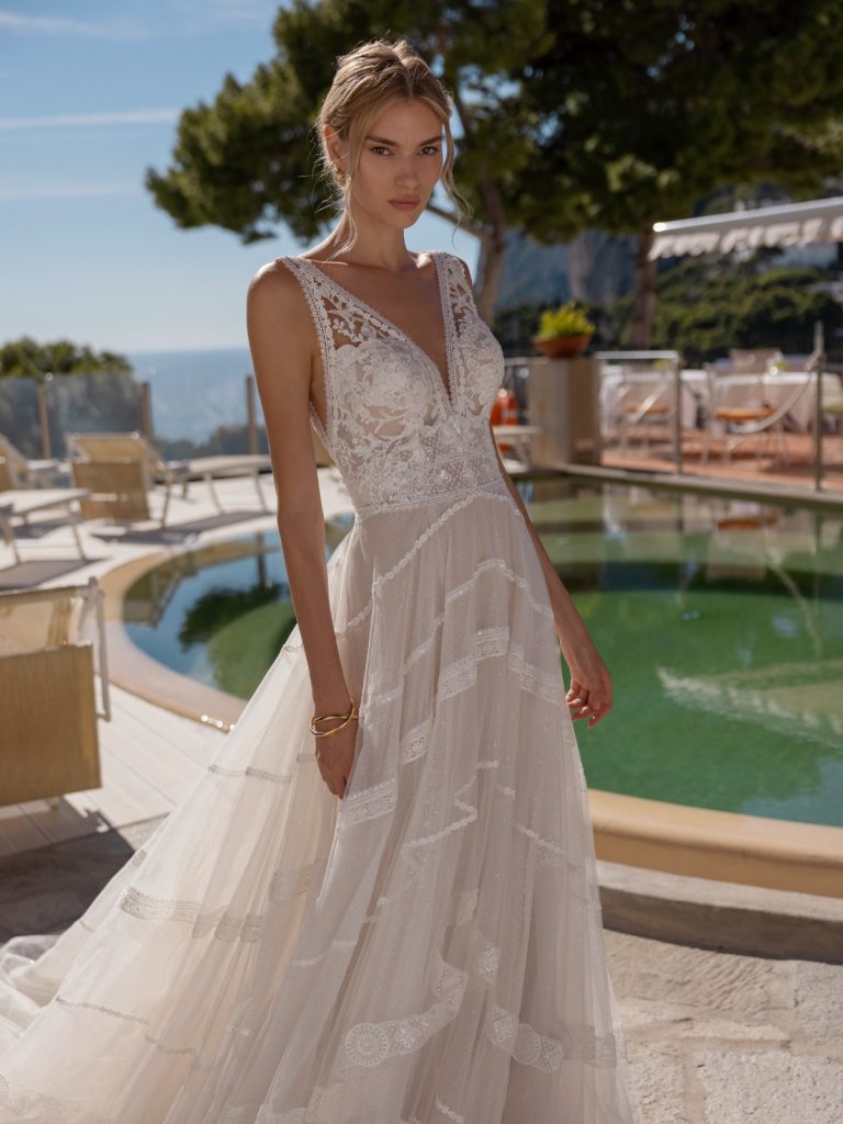 In questa foto una modella posa indossando un abito da sposa Le Papillon by Modeca con gonna in organza a righe e corpetto in pizzo e scollo a V 