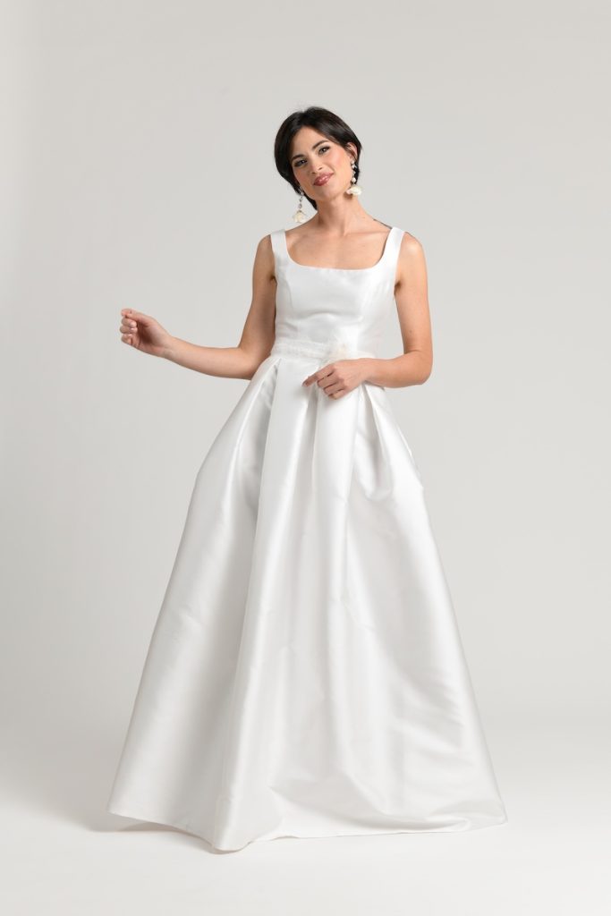 In questa foto una modella posa indossando un abito da sposa ad A in mikado con scollo quadrato disegnato da Benedetta Passalacqua