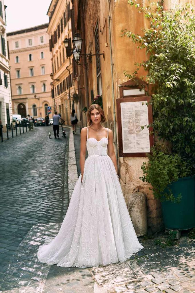 In questa foto una modella posa a Roma indossando un abito da sposa  Atelier Emé 2024 in tulle ricamato con scollo a cuore e bretelline sottili