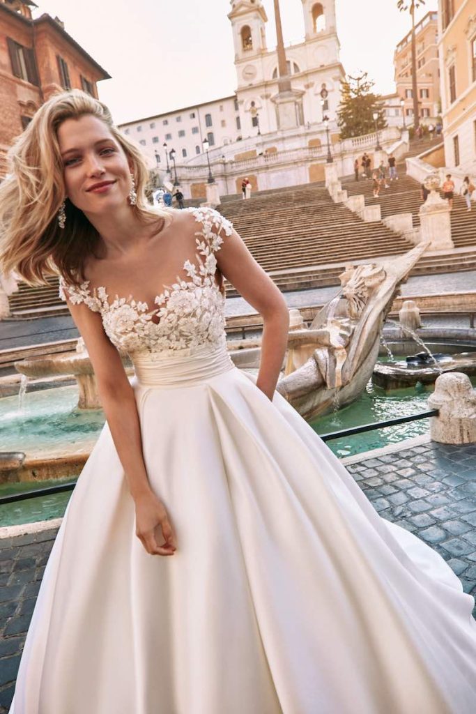 In questa foto una sposa inquadrata a mezzo busto posa a Piazza di Spagna indossando un abito della nuova collezione sposa Atelier Emé 2024 con corpetto ricamato e gonna in mikado