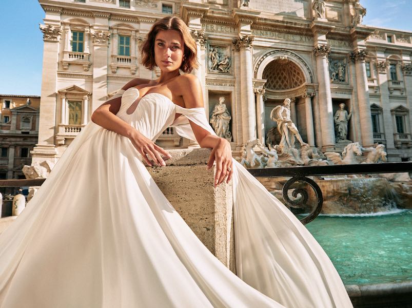 In questa foto una modella posa davanti alla Fontana di Trevi indossando un abito della nuova collezione sposa Atelier Emé 2024