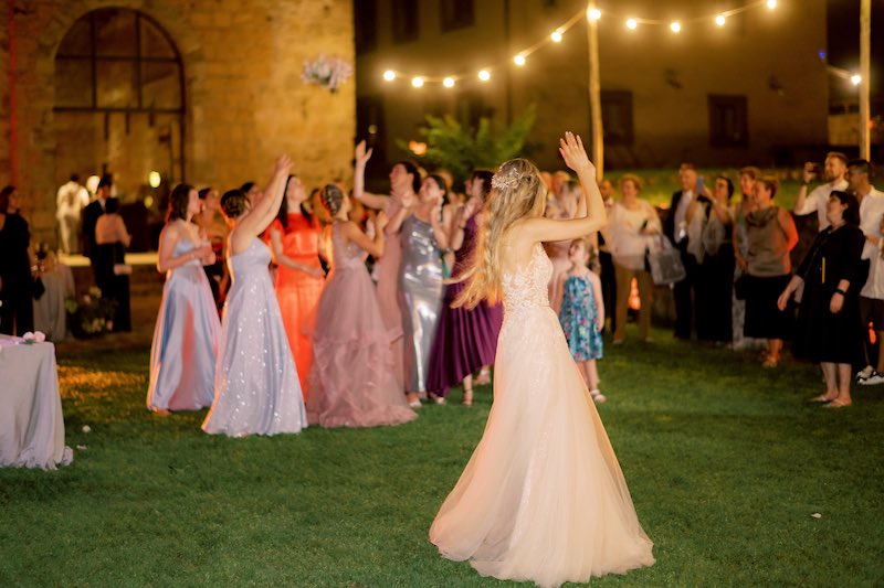 In questa foto una sposa di spalle al lancio del bouquet alle sue ospiti