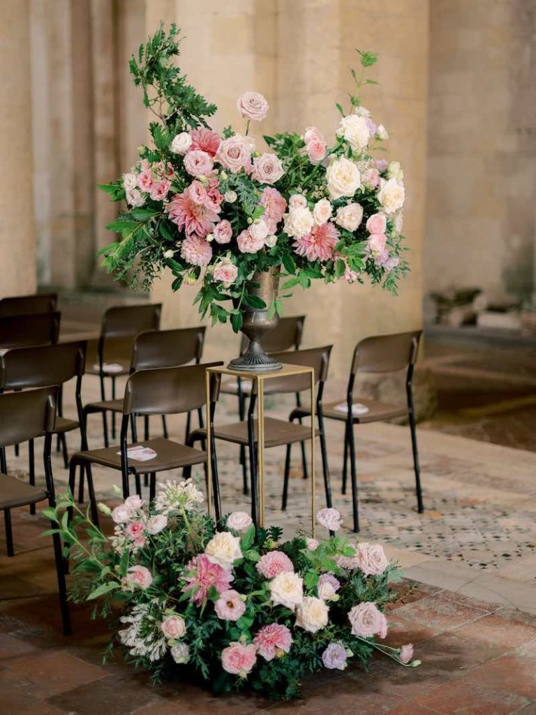 In questa foto due composizioni di fiori di colore rosa e bianco poste all'ingresso della chiesa in vasi e piedistalli di colore oro