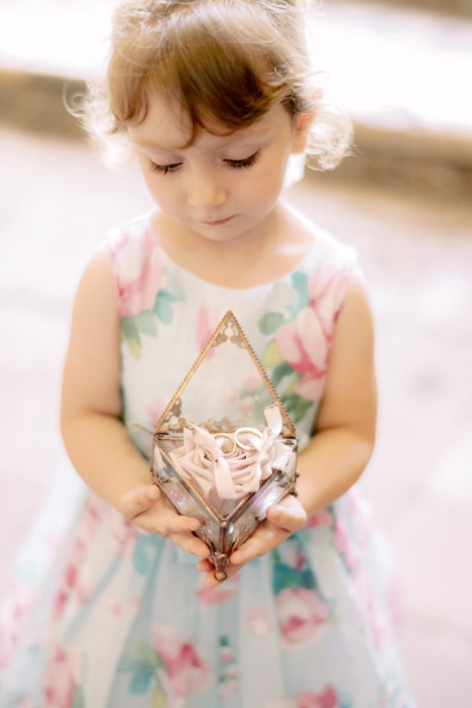 In questa foto una damigella bambina tiene tra le mani un cofanetto portafedi in vetro e metallo a forma di Triforza di "The Legend of Zelda" realizzato per il matrimonio di Gabriele e Cecilia