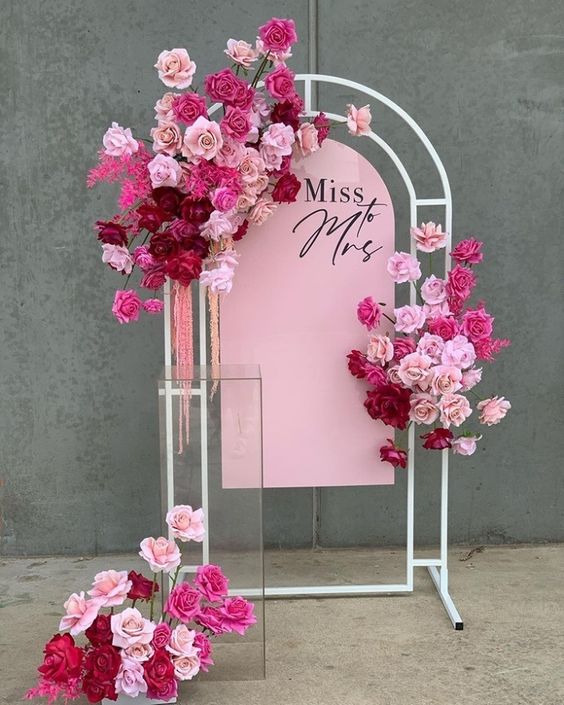 In questa foto un welcome table mariage per un matrimonio stile Barbie con un cartello di colore rosa decorato con rose di colore rosa e fucsia