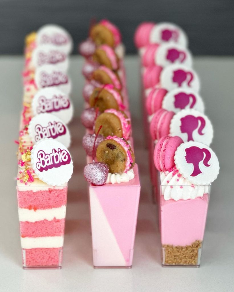 In questa foto tre tipi di dessert da bicchiere per un matrimonio stile Barbie con glassa, macarons e decorazioni con i loghi di Barbie di colore rosa, fucsia e rosa e 
