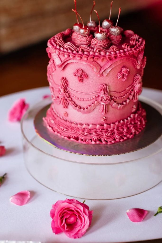 In questa foto una Lambeth Cake con crema al burro di colore fucsia e ciliegine decorate con glitter di colore argento
