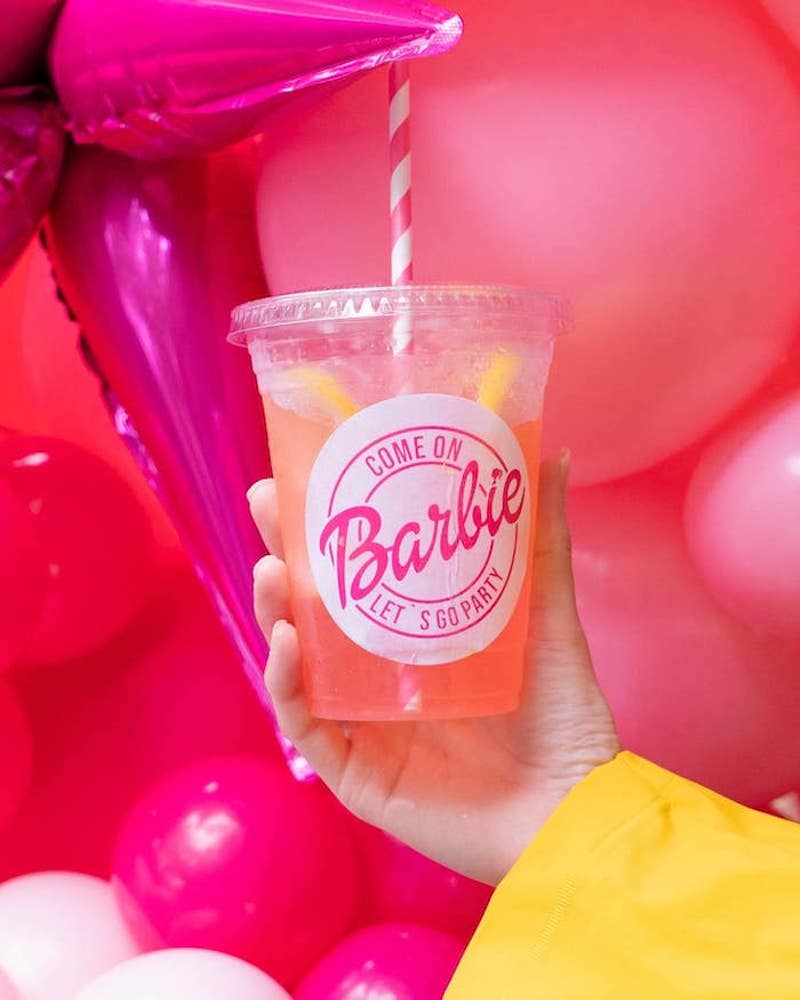 In questa foto un cocktail di colore rosa in bicchiere di plastica personalizzato con scritto "Come on Barbie, let's go party"