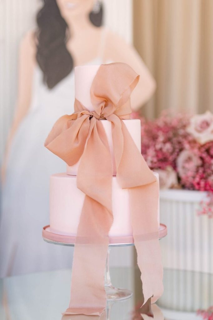 In questa foto una torta a tre piani di colore rosa cipria con nastro di stoffa