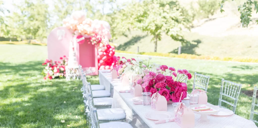 In questa foto un tavolo per matrimonio stile Barbie decorato con fiori fucsia sulla sfondo di un Photobooth a tema